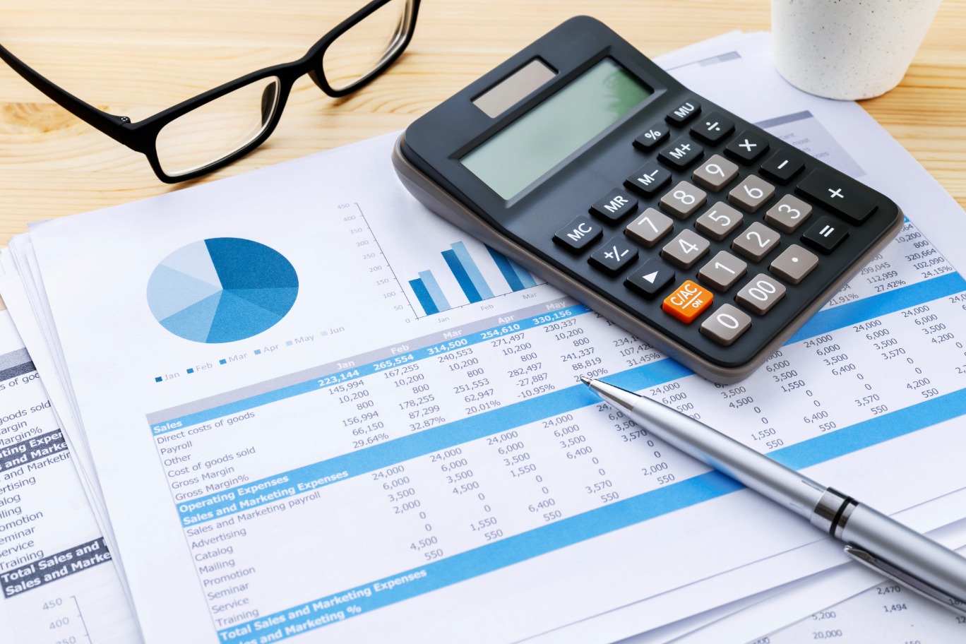 Calculator, glasses, and charts spread across accounting paperwork.
